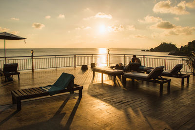 Chairs and table at beach against sky during sunset