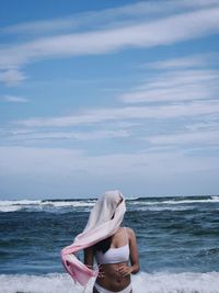 Rear view of woman sitting at beach against sky