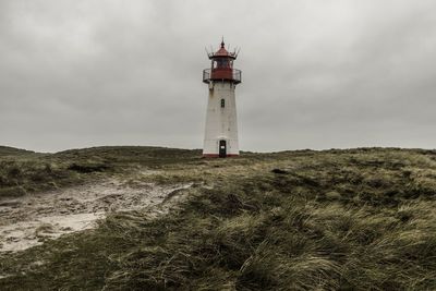 Low angle view of lighthouse on field by building against sky