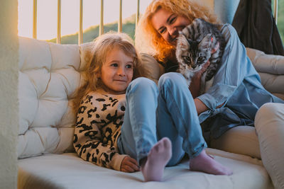 Happy child with smile plays on summer at home with mom, cat at sunset. cat, dog, pets family member