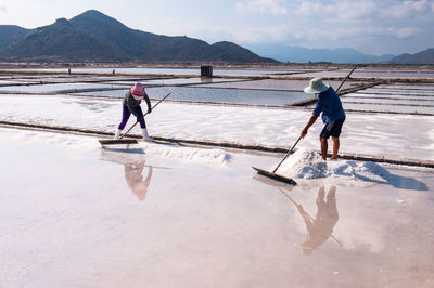 Full length of men fishing in lake against mountains