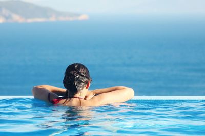 Rear view of woman in swimming pool looking at sea