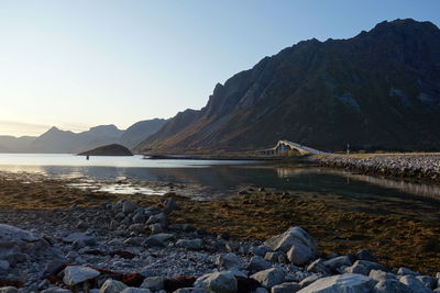 Scenic view of bridge crossing the sea by mountains against clear sky 