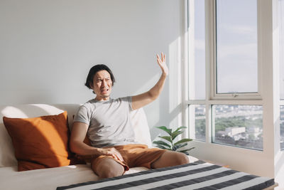 Portrait of young man using mobile phone while sitting on bed at home