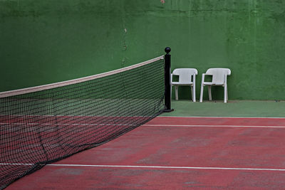 View of tennis court and two empty chairs 