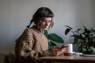 Teen girl sitting at desk reading on-line book, messaging, chatting with friends in smartphone