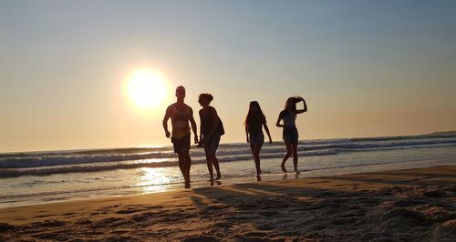 People on beach against clear sky during sunset