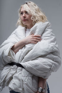 Woman wrapped in blanket standing against gray background