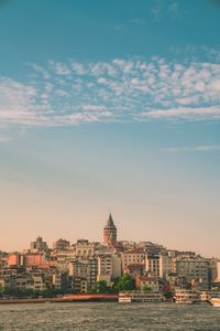 Buildings at waterfront against cloudy sky