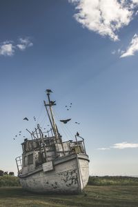 Low angle view of abandoned boat on field against sky