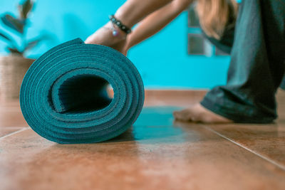 Low section of woman rolling up exercise mat at home