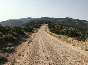 Dirt road leading towards mountains against clear sky