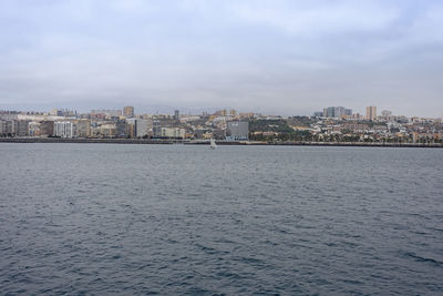 Sea by buildings in city against sky