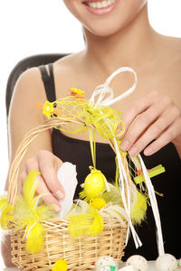 Midsection of young woman decorating wicker basket on table against white background during easter