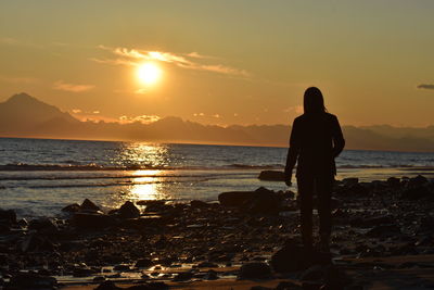 Silhouette man standing on beach against sky during sunset