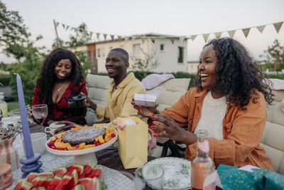 Happy woman holding gift box while laughing with male and female friend in back yard