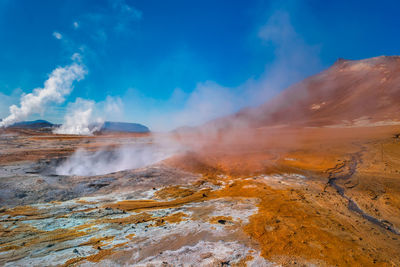 Smoke emitting from volcanic mountain against blue sky