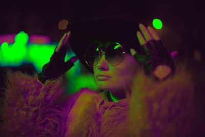 Close-up of woman wearing sunglasses and hat at night