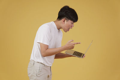 Side view of man holding camera while standing against yellow background