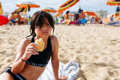 Sitting on the sand beach girl with wet hair holding piece of bread in the hands