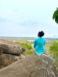 Rear view of man standing on rock against sky