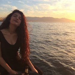 Portrait of beautiful woman sitting by sea during sunset