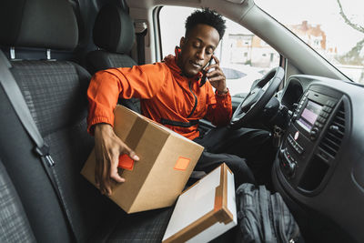 Male driver talking on phone while sitting with packages in delivery van