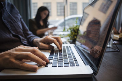 Close-up of businessman using laptop with colleague sitting at table in office