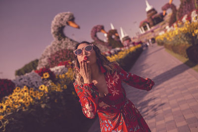 Young woman blowing kiss while standing in ornamental garden at dusk