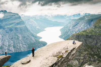 High angle view of people cliff by river against cloudy sky