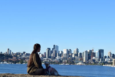 Woman looking at city buildings against clear blue sky