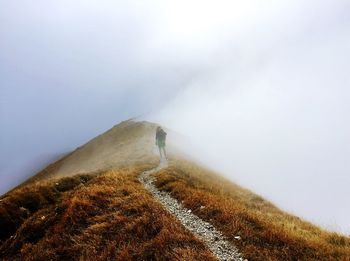 Distant view of people walking on hill against sky during foggy weather