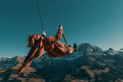 Scenic view of a woman on a giant swing with the mountains against sky
