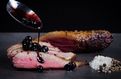 Sauce pouring on smoked meat using spoon against black background