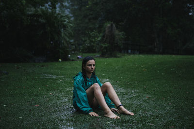A young girl sitting on the grass in the rain during a tropical storm