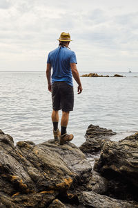 Rear view of man standing on rock by sea against sky