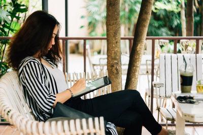 Side view of woman using digital tablet while sitting in cafe