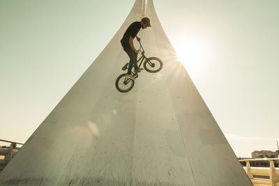 Man riding bicycle on built structure against sky