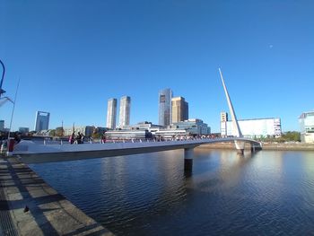 Modern buildings by river against clear blue sky