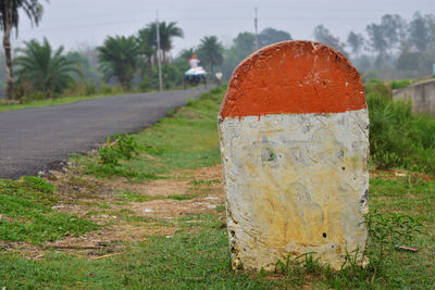 Close-up of blank milestone  beside the road amidst trees on field.