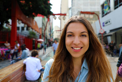 Portrait of smiling young woman against buildings in city