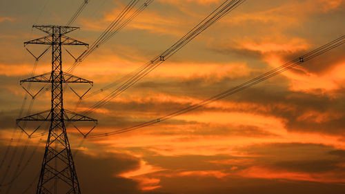 Low angle view of silhouette electricity pylon against dramatic sky