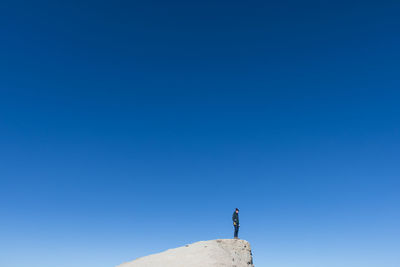 Low angle view of man standing on cliff against clear blue sky