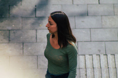 Side view of young woman standing against brick wall