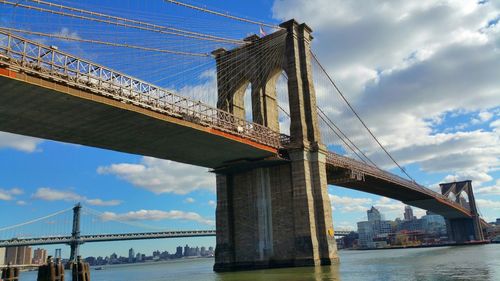 Low angle view of brooklyn bridge over east river against sky in city