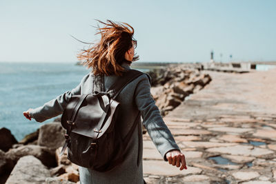 Rear view of woman wearing backpack while standing on pier over sea against clear sky