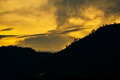 Low angle view of silhouette trees against dramatic sky