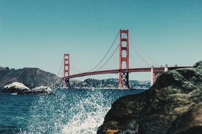 Scenic view of golden gate bridge against clear sky with splashing waves