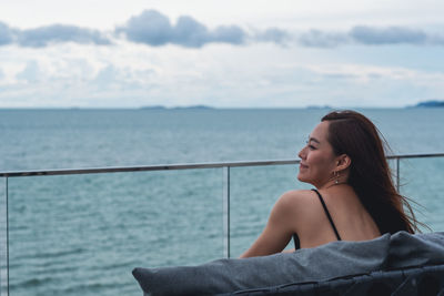 Portrait of young woman sitting on sea against sky