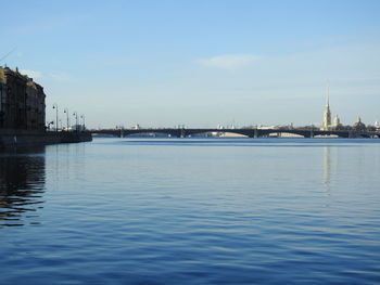 View of buildings by river against blue sky